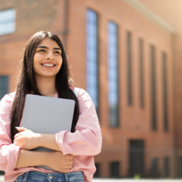 Young woman holding laptop in front of school building
