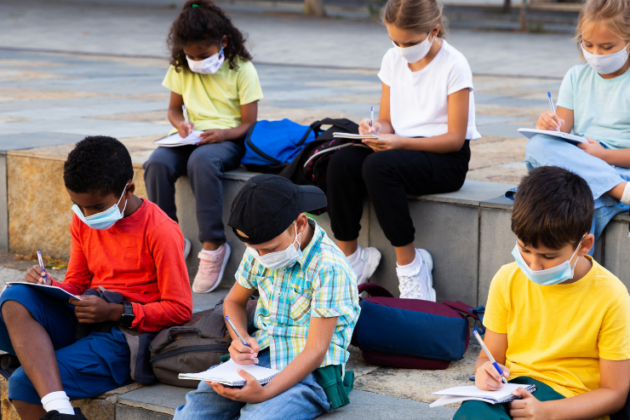 Kids wearing masks and studying outdoors.